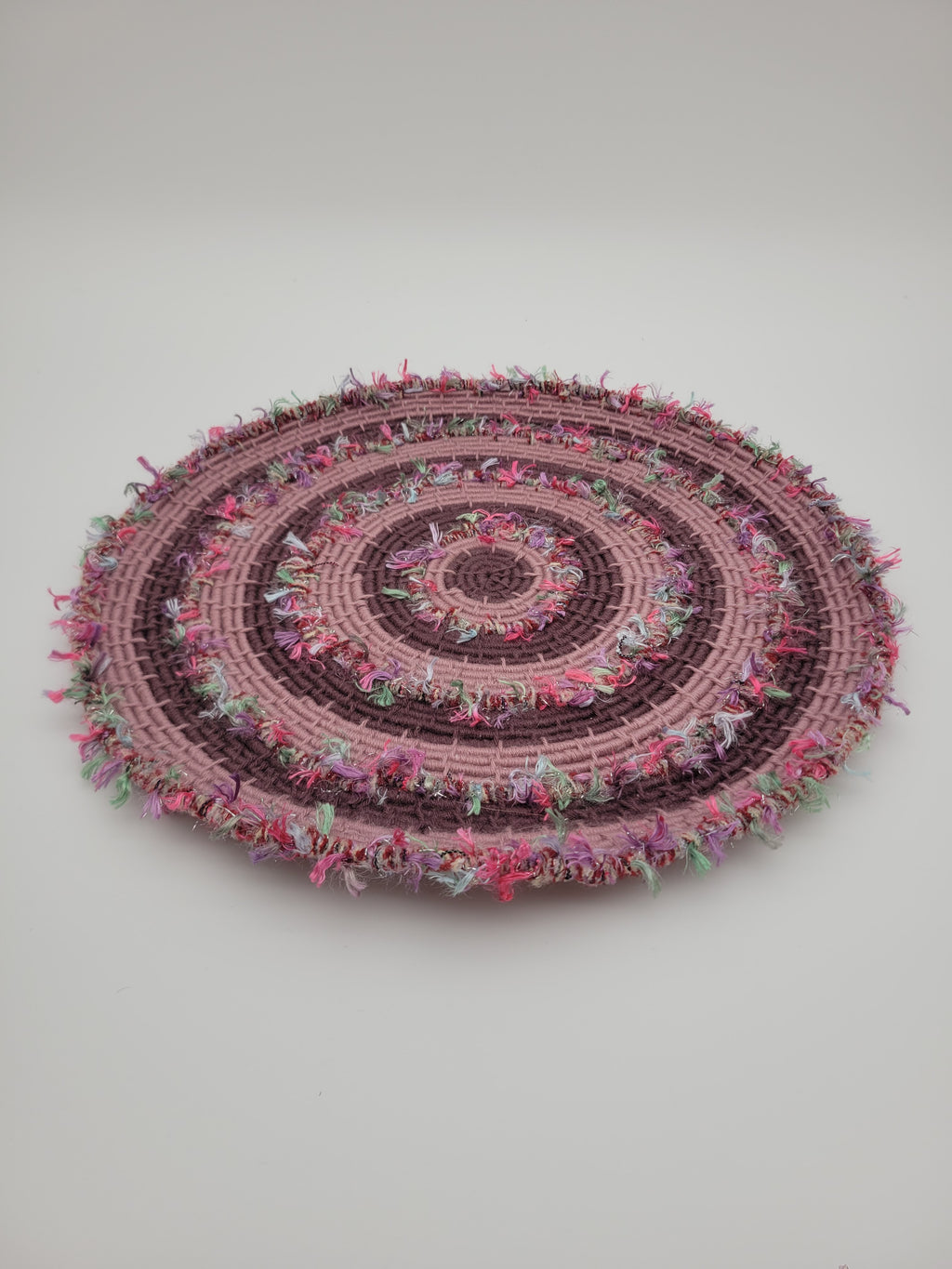 Handmade coiled yarn table centre in pink and soft purple with green highlights