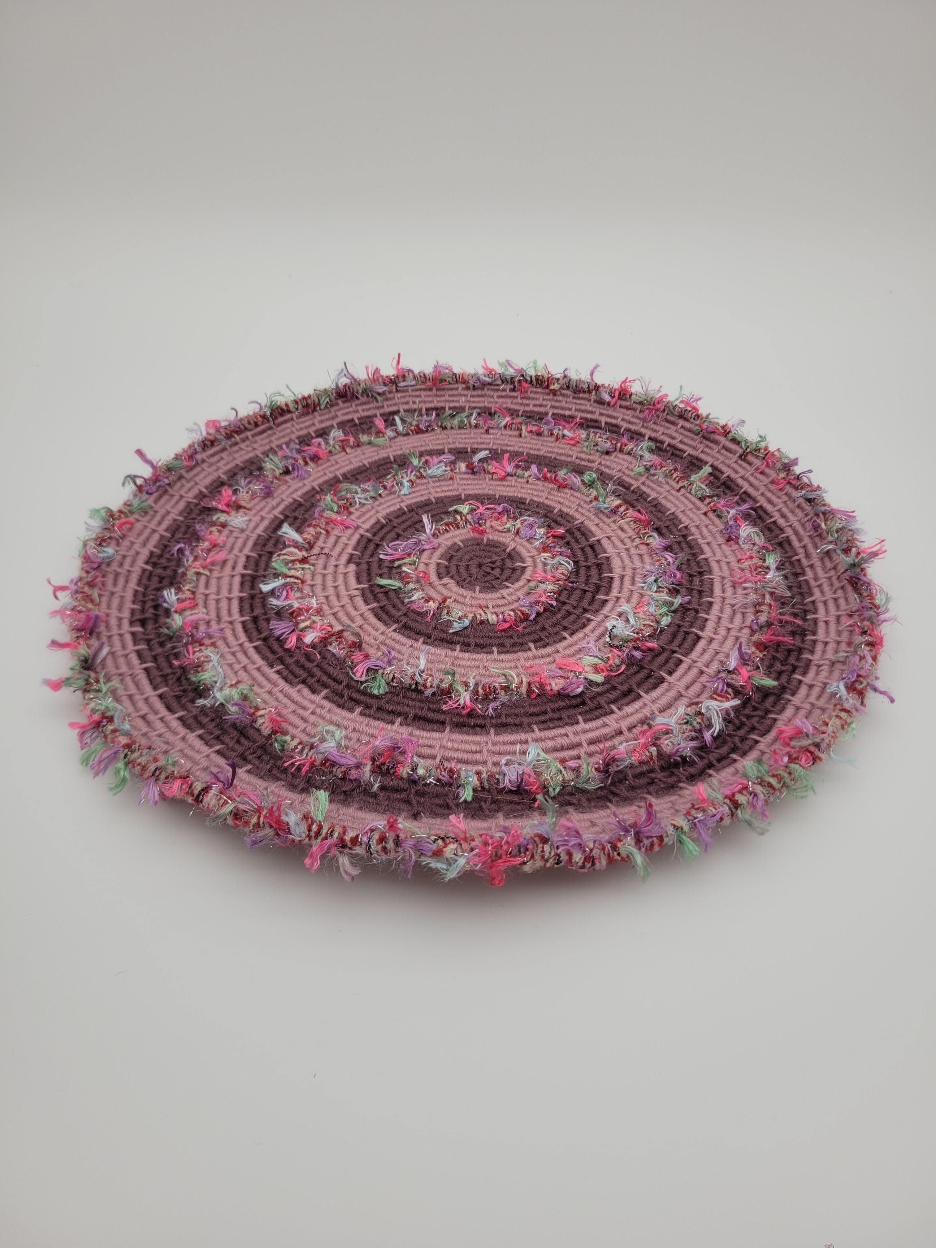 Handmade coiled yarn table centre in pink and soft purple with green highlights