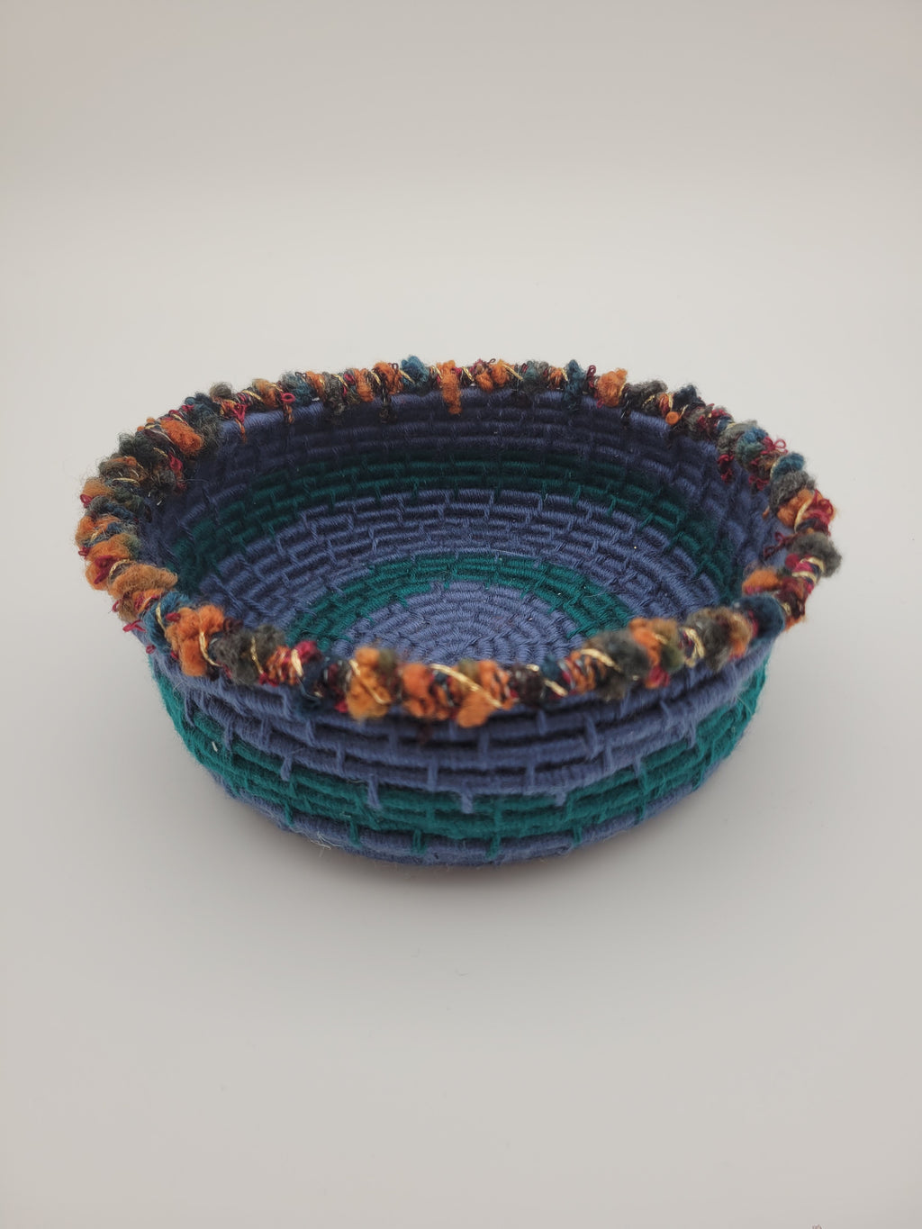 Handmade coiled yarn bowl in blue and green with orange and red details